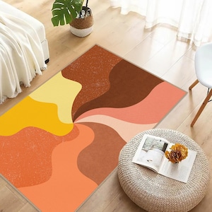 May include: Abstract area rug with a swirling pattern in shades of orange, yellow, brown, and pink. The rug is laid out on a wooden floor.