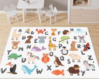 May include: A rectangular area rug featuring a white background with a colorful alphabet pattern. Each letter from A to Z is paired with a cartoon animal illustration, including a llama, crab, fox, elephant, giraffe, penguin, and zebra.