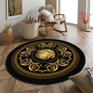 May include: A round black and gold area rug with a decorative pattern featuring a stylized face of Medusa in the center. The rug has a black background with gold accents.