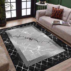 Può includere: Tappeto da area nero e grigio con un design in marmo bianco e un bordo argentato a chiave greca. Il tappeto ha un motivo a rombi sullo sfondo.