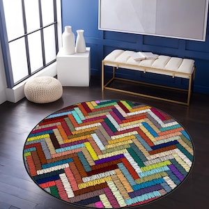 May include: A round, colourful rug with a geometric pattern of zigzags and stripes in shades of red, orange, yellow, green, blue, purple, and brown. The rug has a black border.