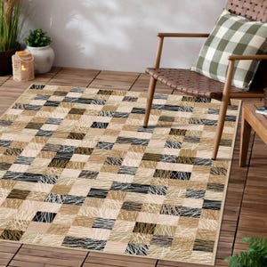 May include: Rectangular area rug with a geometric pattern in shades of beige, tan, and black. The rug features a patchwork design with textured lines and shapes, creating a modern and stylish look. The rug is placed on a wooden deck.