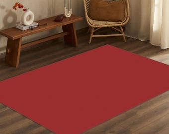 May include: A solid, deep red rectangular area rug with a smooth, uniform texture. The rug is positioned flat on a dark brown wooden floor, covering a large portion of the foreground and extending towards the centre of the room.