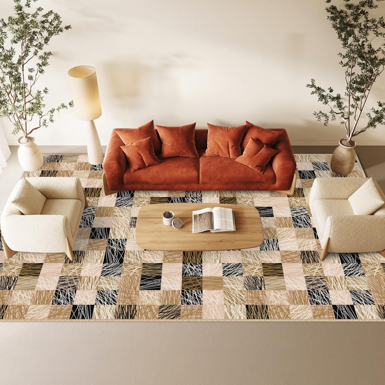 May include: An overhead view of a living room arrangement. A rust-coloured sofa with matching cushions, two cream armchairs, and a wooden coffee table are visible. The floor is covered by a patterned rug with squares of beige, black, and white threads. Decorative plants and a floor lamp complete the scene.