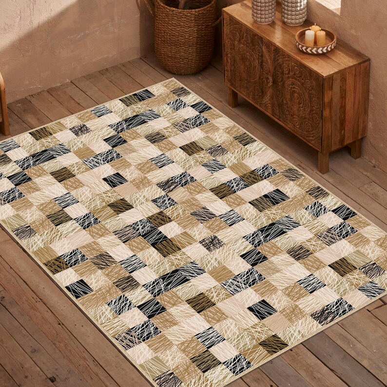 May include: Rectangular rug with a patchwork design. The rug features squares in beige, black, and brown tones, with white linear accents. The rug is placed on a wooden floor, creating a neutral and modern aesthetic.