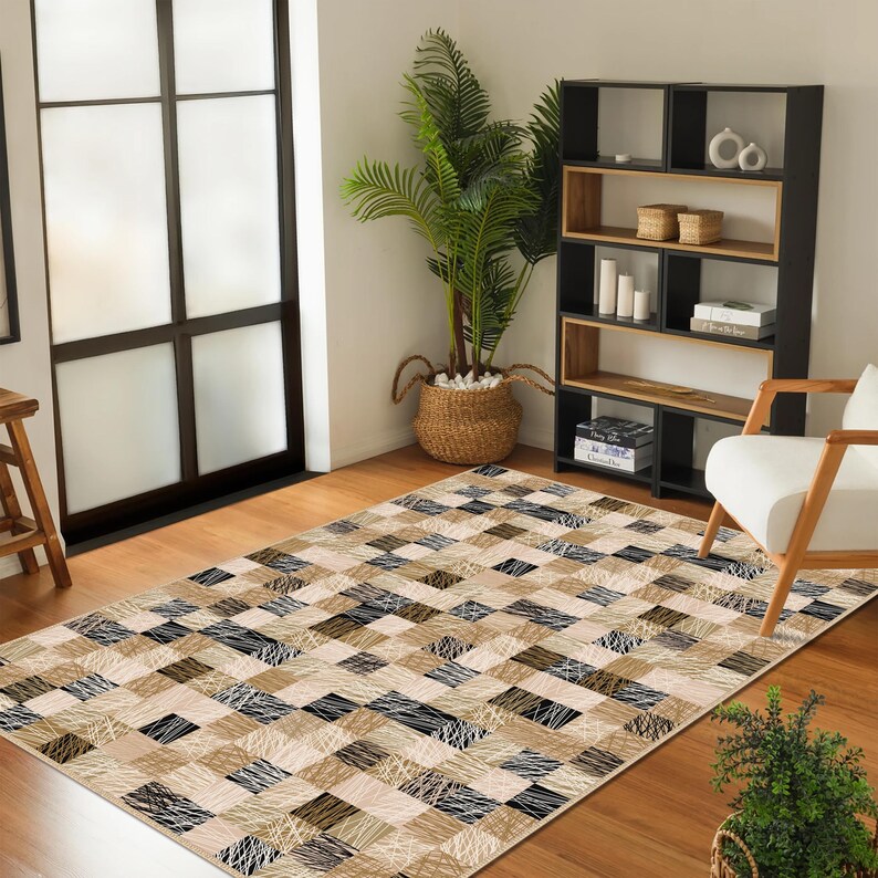 May include: A rectangular rug featuring a geometric pattern of squares in beige, black, and white. The rug has a textured appearance with a mix of solid and line-drawn designs. The rug is placed on a wooden floor.