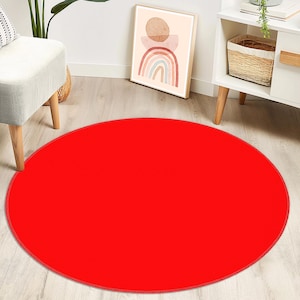 May include: A solid, vibrant red circular area rug with a smooth, uniform texture and a matching red stitched border. The rug is positioned flat on a light-colored wooden floor, providing a bold, singular color accent to the surrounding space.