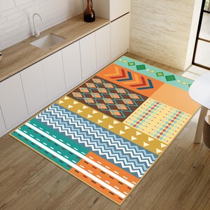 May include: A rectangular area rug featuring a patchwork design of geometric patterns in vibrant colors including orange, teal, yellow, brown, and white. The rug displays various motifs such as chevrons, diamonds, stripes, and triangles.