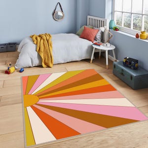 Könnte beinhalten: Ein bunter Teppich mit einem Sonnenstrahlen-Design in Orange-, Rosa-, Braun- und Gelbtönen. Der Teppich hat einen weißen Hintergrund und eine gelbe Sonne in der Mitte.