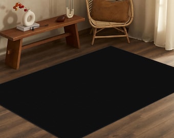 May include: A black area rug on a hardwood floor. The rug is in a living room setting with a wooden bench and a wicker chair.