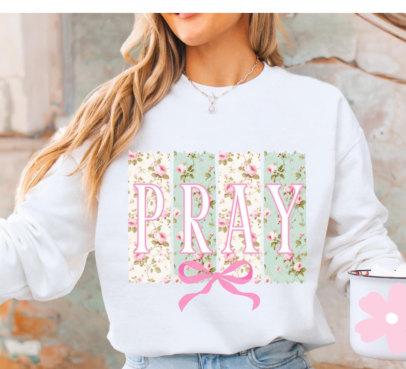 May include: White sweatshirt with a floral print and the word "PRAY" in pink letters. A pink bow is centered below the word.