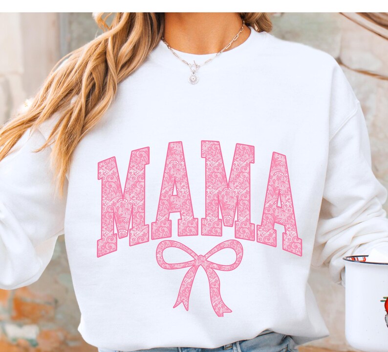 May include: White sweatshirt with a pink "MAMA" graphic in a patterned font with a pink bow underneath.
