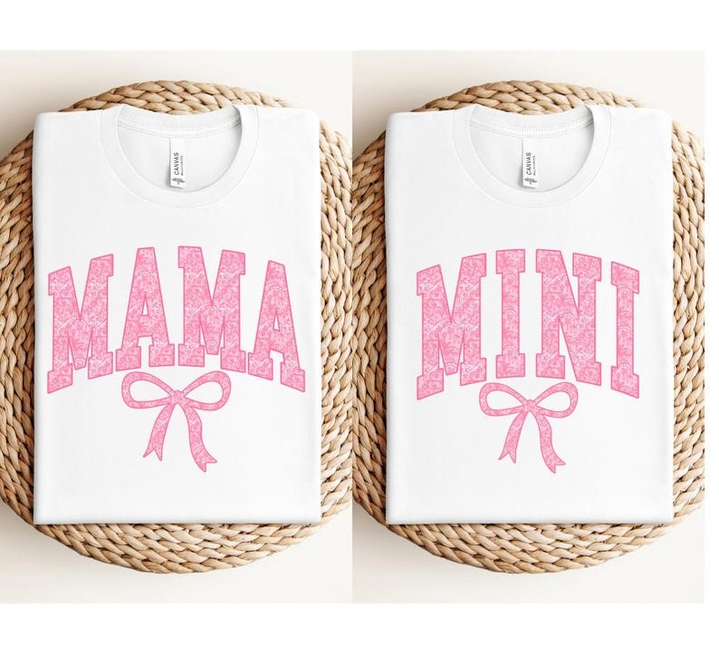 May include: Two white t-shirts with pink text. The first shirt says "MAMA" with a pink bow underneath. The second shirt says "MINI" with a pink bow underneath.