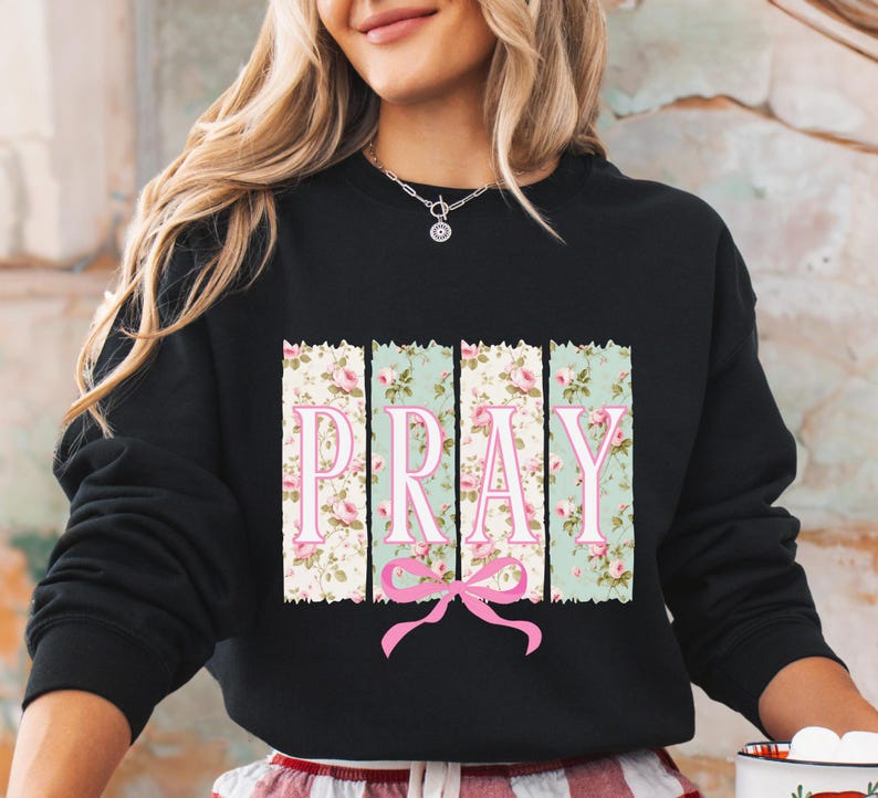 May include: Black sweatshirt with a floral print and the word "PRAY" in pink letters. The floral print is in shades of green, pink, and white.
