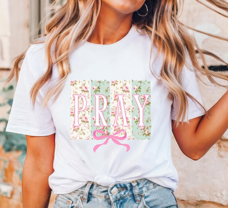 May include: White t-shirt with a floral print design and the word "PRAY" in pink letters. A pink bow is below the word.