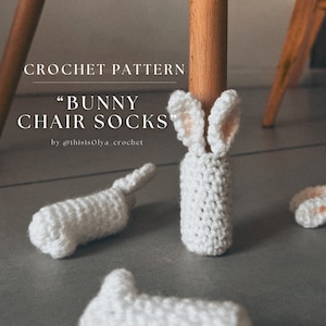 May include: Crochet pattern for "Bunny Chair Socks" by @thisisOlya_crochet. The image shows four white crocheted bunny chair socks, with two of them on a wooden chair leg.