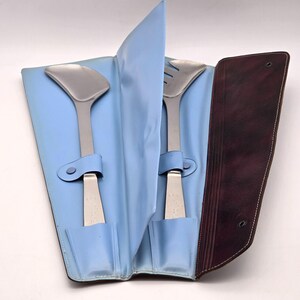 May include: A set of two silver serving utensils in a blue and brown leather case. The utensils are a slotted spoon and a serving spoon.