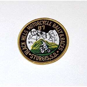 May include: Embroidered patch with a gold border featuring the text "Black Hills Motorcycle Rally & Races" and "Sturgis, S.D." The patch includes an image of Mount Rushmore and a motorcycle. The year "87" is also displayed.