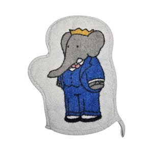 May include: A white towelling bath mitt featuring an embroidered illustration of a grey elephant wearing a blue suit, a pink bowtie, and a yellow crown. The elephant is depicted standing upright with its trunk curved to the left side.
