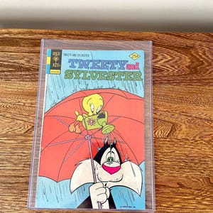 May include: A vintage comic book cover featuring Tweety Bird and Sylvester the Cat. The cover is blue with a red umbrella and a yellow bird holding a watering can. The title of the comic is "Tweety and Sylvester" and the price is 25 pence.