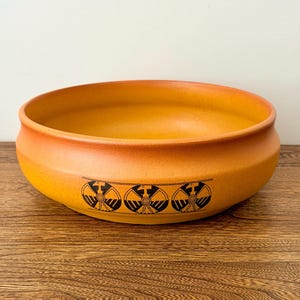 Peut inclure: Un bol rond en céramique orange avec un large bord. Le bol présente un motif géométrique noir décoratif sur l'extérieur. Le bol est posé sur une surface en bois.