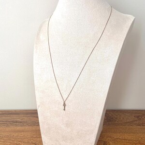 May include: A silver necklace with a key pendant, displayed on a white jewellery bust. The key pendant is detailed, and the chain is delicate. The bust is set against a light background and a wooden surface.