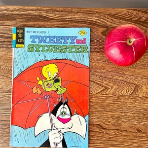 May include: A vintage comic book cover featuring Tweety Bird and Sylvester the Cat. The cover is blue with a red umbrella and rain. The title is "Tweety and Sylvester" with the price "25c" in a diamond shape. The comic book is from "Gold Key" comics.
