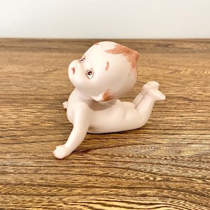Figurka lalki Kewpie z biskwitu, leżąca na brzuszku, 4"x3", rude włosy, ręcznie malowane oczy, nieszkliwiona porcelana, raczkujące dziecko