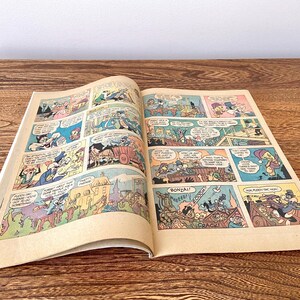 May include: A vintage comic book featuring a cartoon character with a red hat and a blue shirt. The comic book is open to a page with a panel showing the character riding a horse. The comic book is in good condition with some wear and tear.