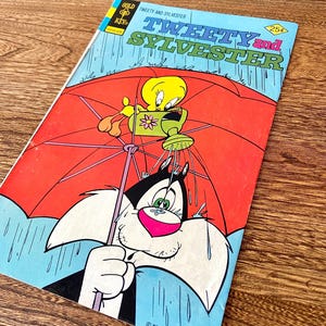 May include: A vintage comic book cover featuring Tweety Bird and Sylvester the Cat. Tweety is holding a watering can and Sylvester is under a red umbrella. The cover is blue and has the title "Tweety and Sylvester" in yellow and red letters. The comic book is from the Gold Key Comics series.