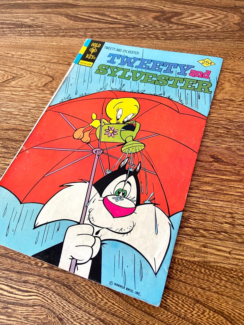 May include: A vintage comic book cover featuring Tweety Bird and Sylvester the Cat. Tweety is holding a watering can and Sylvester is under a red umbrella. The cover is blue and has the title "Tweety and Sylvester" in yellow and red letters. The comic book is from the Gold Key Comics series.