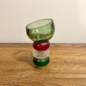 Peut inclure: Un bol en verre vert posé sur une pile de trois ornements ronds. Les ornements sont rouges, blancs avec des volutes dorées et verts. Les ornements ont des accents dorés.