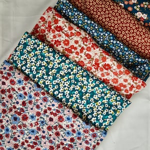 Peut inclure: Six carrés de tissu empilés avec différents motifs floraux. Les tissus sont dans des tons de rouge, bleu, vert et blanc.