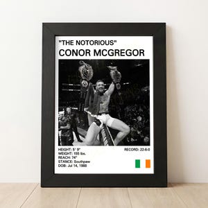 May include: Black and white framed print featuring Conor McGregor holding championship belts. Text at the top reads "THE NOTORIOUS" CONOR MCGREGOR. Stats include height 5' 9", weight 155 lbs, reach 74", and record 22-6-0.