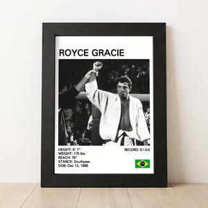May include: Black and white framed print featuring Royce Gracie, with his height at 6' 1", weight 175 lbs, and reach at 76". The print includes his record, stance, and date of birth. A Brazilian flag is in the lower right corner.