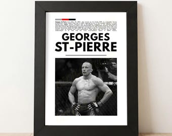 May include: Black framed print featuring Georges St-Pierre, a Canadian mixed martial artist. The print includes a black and white photo of St-Pierre in the ring, with his name in large, bold letters above the image. Text details his career.
