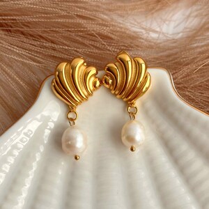 May include: Gold tone earrings with a textured shell design and a single pearl drop on each earring.
