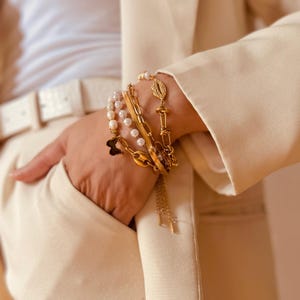 May include: A set of gold bracelets with different chain styles, including a pearl bracelet, a chain with a butterfly charm, and a chain with a lip-shaped charm with rhinestones.