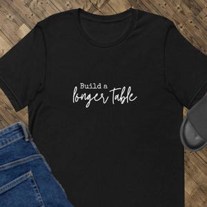 May include: Black t-shirt with white text that reads "Build a longer table".