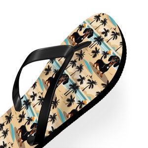 May include: Flip-flop with a black strap and a beach-themed design. The pattern includes cartoon dachshunds, palm trees, surfboards, and a sandy beach background. The flip-flop is white on the bottom.