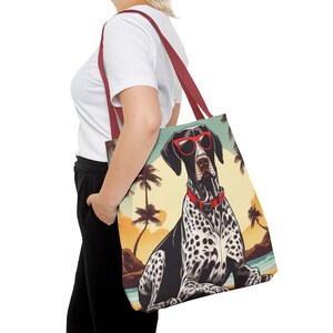 May include: A red and white tote bag with a black and white dog wearing sunglasses and a red collar. The dog is sitting on a beach with palm trees in the background. The bag has a red handle.
