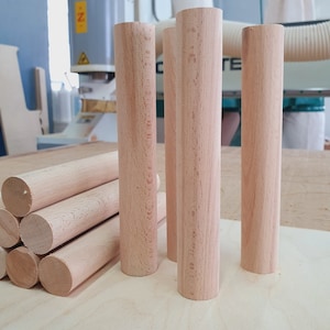 May include: Four wooden dowels, each about 10 inches long, are arranged in a row on a light wood surface. The dowels are all the same size and shape, and they are made of a light-colored wood.