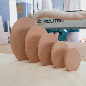 May include: Five wooden circles of varying sizes, arranged from largest to smallest, on a light wood surface. The circles are all a light brown color and have a smooth, polished finish.