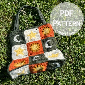May include: A crochet tote bag with a green, orange, white, and yellow color scheme. The bag features a repeating pattern of stars, moons, and suns. The bag is on a bed of green grass with white flowers. The text "PDF PATTERN MARIA FLORA" is visible in the upper right corner of the image.