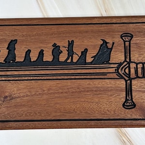 May include: A wooden sign with a black silhouette of a sword and a group of figures walking towards it. The sword is the iconic sword from the Lord of the Rings, and the figures are the hobbits from the story.