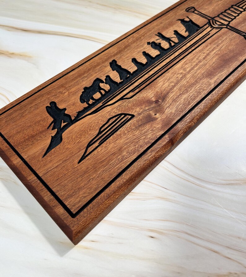 May include: A wooden sign with a black outline and a design of a sword and a line of figures walking towards it. The design is reminiscent of the Lord of the Rings.