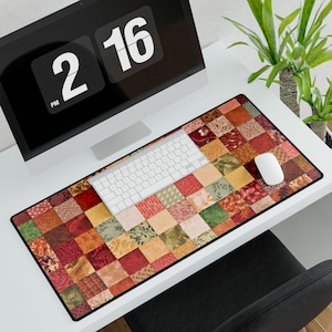 May include: A rectangular desk mat with a patchwork quilt design in shades of red, orange, green, and beige. A white keyboard and mouse sit on the mat, with a computer monitor in the background. The mat measures approximately 36 inches long.