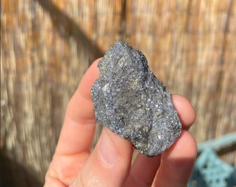 May include: A rough, gray and silver rock with a metallic sheen. The rock has a jagged, irregular shape.