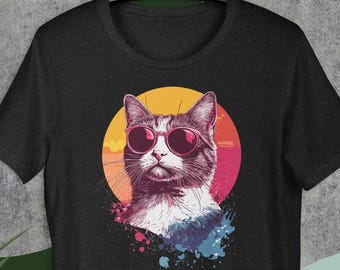 May include: Black t-shirt featuring a cat wearing sunglasses, set against a sunset-colored circle. The cat illustration has a retro, vintage style, with colorful paint splatters below the cat's head. The shirt is hanging on a black hanger.