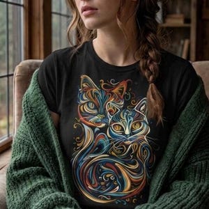 以下が含まれることがあります： 2匹の猫のカラフルで芸術的なデザインが施された黒いTシャツ。デザインは、青、オレンジ、黄色、緑の色合いの渦巻き線を使用しています。緑色のニットカーディガンを着て、お茶のマグカップを持っています。